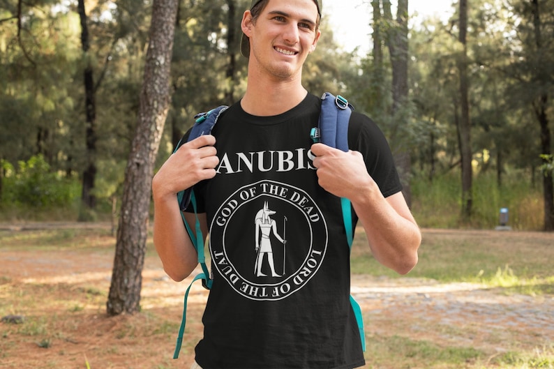 Op de afbeelding: Een zwart T-shirt met een witte afbeelding van Anubis, de Egyptische god van de dood. De afbeelding is een cirkel met de woorden "God van de Doden" en "Heer van de Duat" rondom de afbeelding van Anubis.