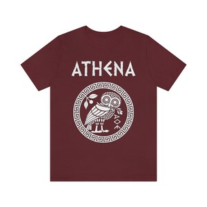 May include: A maroon t-shirt with a white graphic of the Greek goddess Athena's owl with the text "ATHENA" above it.