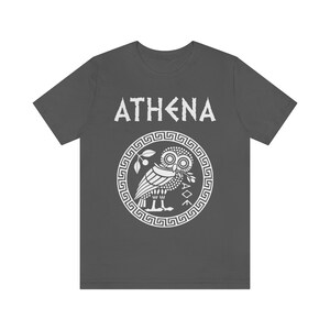 May include: A dark gray t-shirt with a white graphic of the Greek goddess Athena's owl and the word "ATHENA" in white.