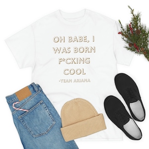 Könnte beinhalten: Weißes T-Shirt mit dem Aufdruck "Oh babe, I was born f*cking cool -Team Ariana" in Gold.