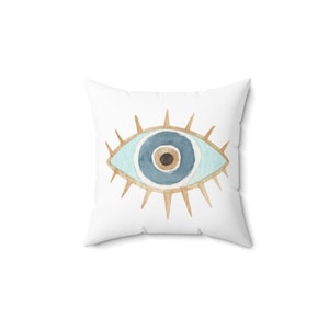 May include: White pillow with a blue evil eye design. The eye is surrounded by gold rays.