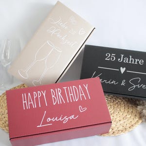 Könnte beinhalten: Drei Geschenkboxen mit unterschiedlichen Designs. Die erste Box ist beige mit einer silbernen Aufschrift, die "Liebe zu Hochzeit" lautet. Die zweite Box ist schwarz mit einer silbernen Aufschrift, die "25 Jahre Karin & Sven" lautet. Die dritte Box ist rot mit einer weißen Aufschrift, die "Happy Birthday Louisa" lautet.