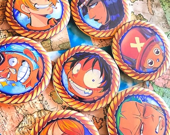 Puede incluir: Seis botones redondos, coloridos, de personajes de dibujos animados con un borde de cuerda. Los personajes son del anime One Piece. Los personajes son Luffy, Zoro, Nami, Sanji, Chopper y Usopp.