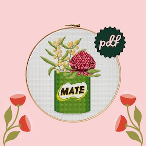 May include: Cross stitch pattern featuring a green can with the word "MATE" on it, filled with red and yellow flowers. The pattern is in a wooden embroidery hoop.