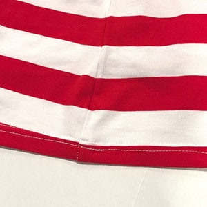 May include: Close-up of the hem of a red and white striped shirt. The hem is sewn with a white thread.