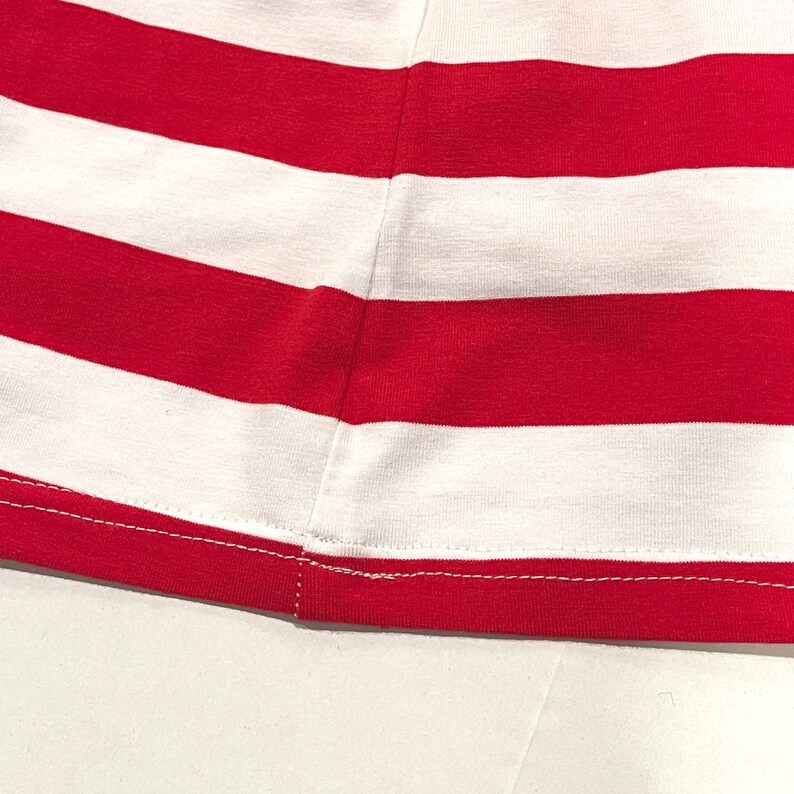 May include: Close-up of the hem of a red and white striped shirt. The hem is sewn with a white thread.