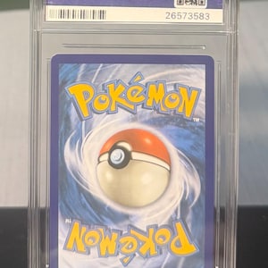 May include: A graded Pok&eacute;mon trading card encased in a clear plastic holder. The card features the Pok&eacute;mon logo and a Pok&eacute; Ball design on a blue background. The holder has the PSA logo and a serial number.