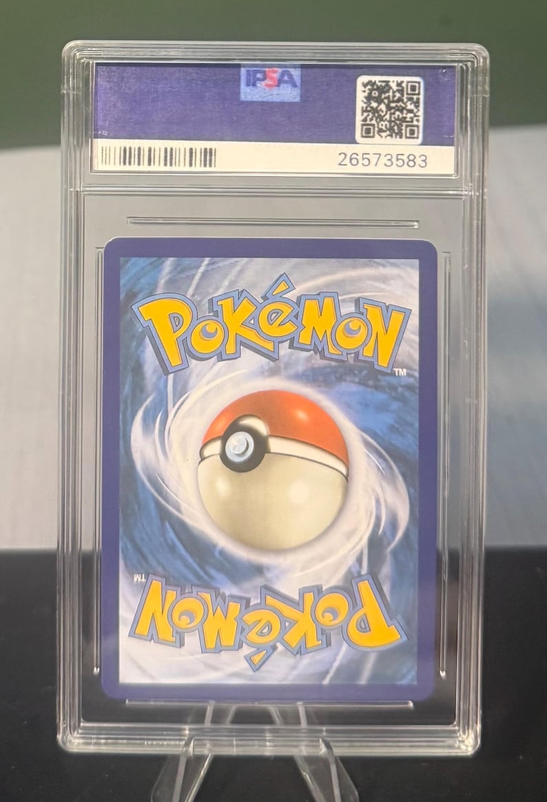 May include: A graded Pok&eacute;mon trading card encased in a clear plastic holder. The card features the Pok&eacute;mon logo and a Pok&eacute; Ball design on a blue background. The holder has the PSA logo and a serial number.