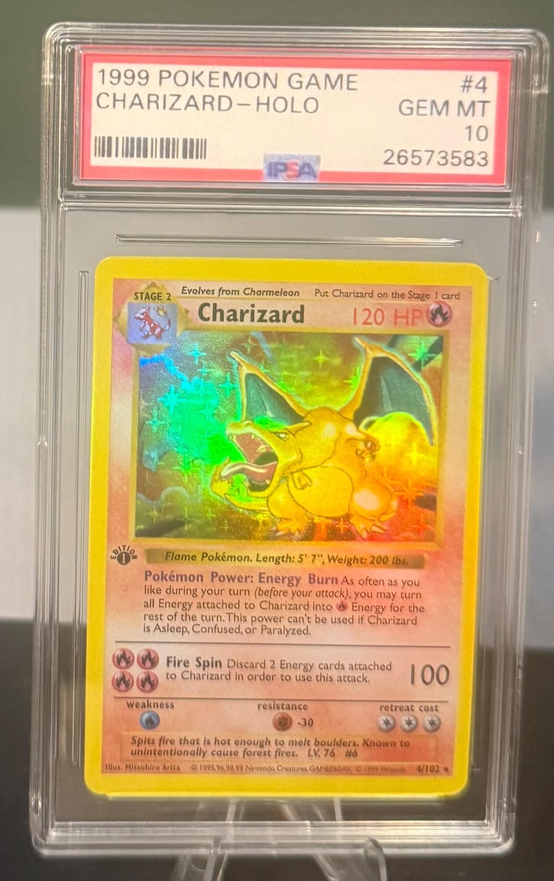 May include: A graded 1999 Pok&eacute;mon Game Charizard-Holo card. The card features a holographic image of Charizard, a flame Pok&eacute;mon, with a length of 5' 7" and a weight of 200 lbs. The card is encased in a protective case.