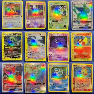 May include: A collection of 24 holographic Pokemon trading cards featuring various characters and illustrations. The cards are arranged in four rows of six cards each. The cards are all in good condition and have a shiny, holographic finish.