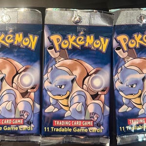 May include: Three identical blue Pokémon Trading Card Game booster packs featuring the character Blastoise. Each pack displays the yellow Pokémon logo at the top and the text 11 Tradable Game Cards at the bottom, with a metallic silver seal.