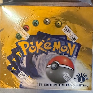 May include: A sealed yellow Pokémon trading card game booster box featuring the Wizards of the Coast logo, a red and white Poké Ball graphic, and the text 1st Edition Limited Printing. The box displays various elemental energy symbols.