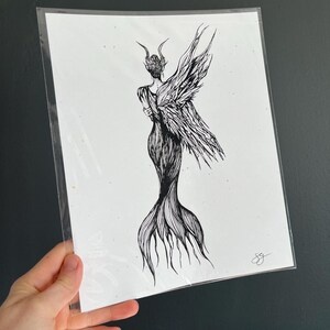 May include: Black and white line art print of a woman with wings and a tail, standing with her back to the viewer. The print is on a white background.