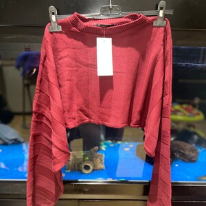 Könnte beinhalten: Ein weinroter, verkürzter Pullover mit langen Ärmeln. Der Pullover hat eine gerippte Struktur und einen runden Ausschnitt.