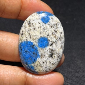 May include: Oval cabochon gemstone with a white and black speckled background and blue spots.