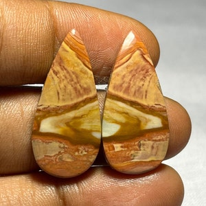 May include: Pair of teardrop-shaped cabochons with a layered pattern of brown, orange, and white colors. The stones have a polished finish.