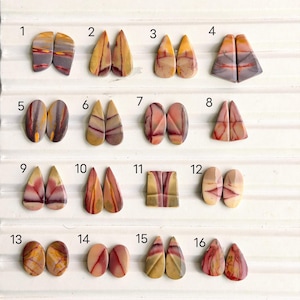 May include: Sixteen pairs of polished, multicolored cabochons arranged in a grid, numbered 1 through 16. Each pair features unique natural patterns in shades of yellow, red, purple, and tan, with shapes including teardrops, ovals, and rectangles.