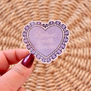 May include: A heart-shaped sticker with a lavender background and the words "Dearest Gentle Reader" in elegant script. The sticker is outlined with a decorative border and held against a woven background.