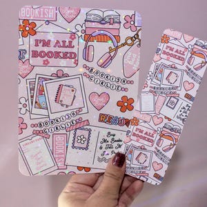 May include: A pink and white bookish-themed notebook and bookmark set. The notebook and bookmark feature illustrations of books, hearts, flowers, and the text "I'M ALL BOOKED". The set has a cute, girly aesthetic, perfect for book lovers.