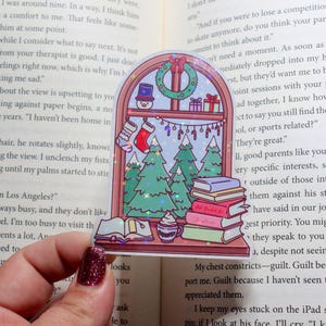 May include: A sticker depicting a festive window scene with a wreath, snowman, and stocking. The window reveals green Christmas trees and a stack of books. A small dessert sits on the windowsill.