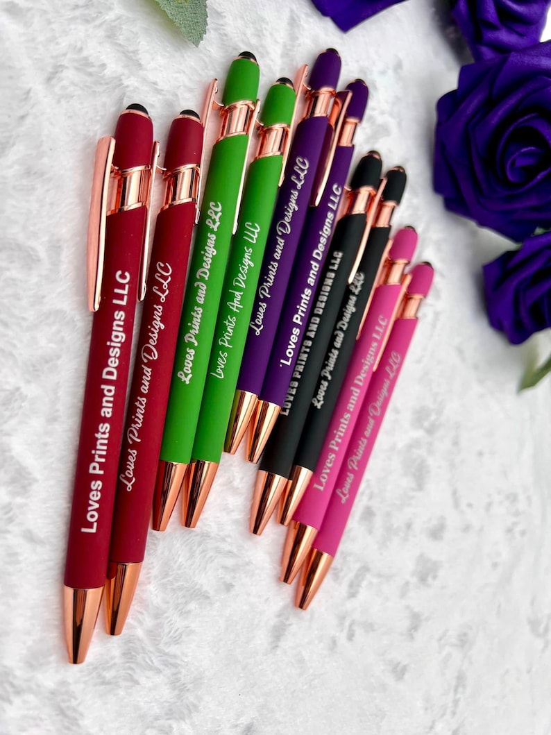 Pu&ograve; includere: Un gruppo di dieci penne con dettagli in oro rosa e una punta a stilo. Le penne sono di vari colori, tra cui rosso, verde, viola, nero e rosa. Ogni penna &egrave; incisa con il testo "Loves Prints and Designs LLC".