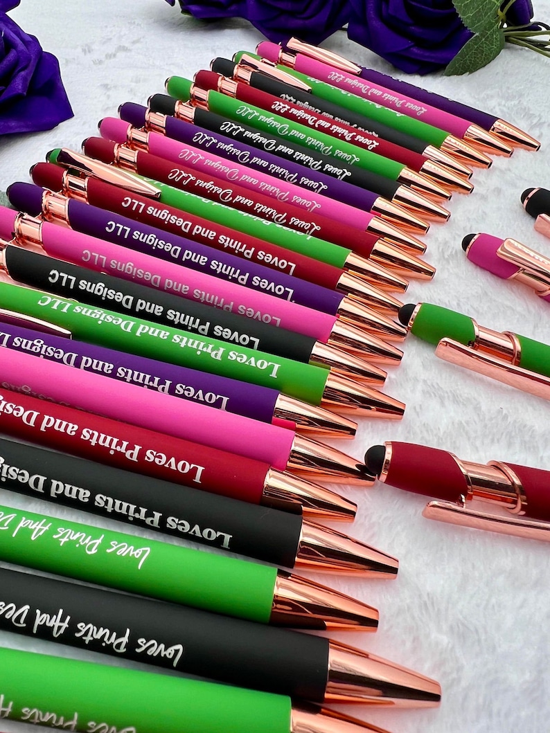 Pu&ograve; includere: Una collezione di penne con dettagli in oro rosa e una variet&agrave; di colori, tra cui verde, viola, rosa e nero. Ogni penna &egrave; incisa con il testo "Loves Prints and Designs LLC".