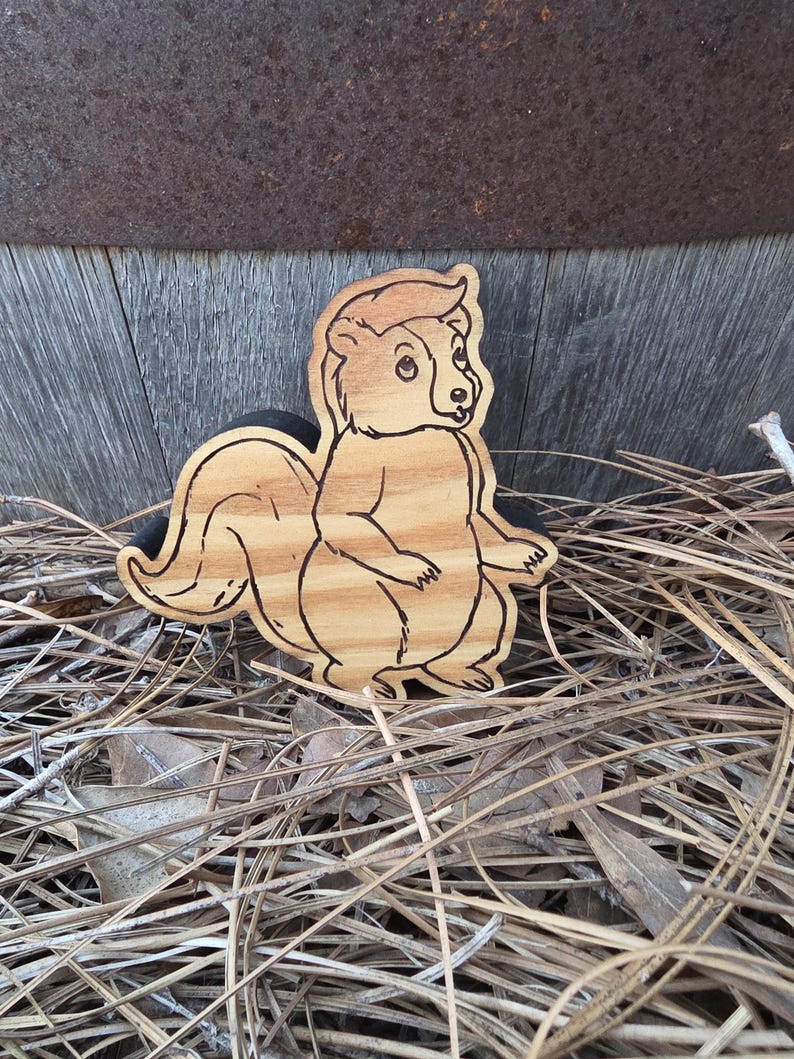 May include: A flat, light brown wooden cutout shaped like a cartoon squirrel. The squirrel is depicted in profile with a large, bushy tail, small ears, and a detailed outline burned into the wood grain, showing a standing posture with front paws.