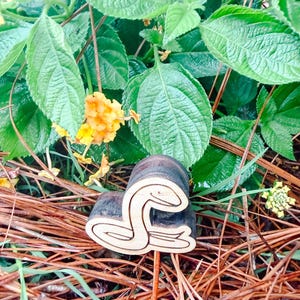 May include: A dark brown wooden stamp featuring a carved snake design on its face. The stamp has a cylindrical handle and a flat base with the snake outline clearly etched into the wood, showing a coiled body and a raised head profile.