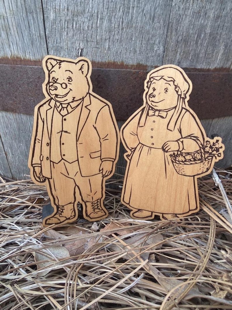 May include: Two light brown wooden cutouts featuring laser-engraved illustrations of anthropomorphic bears. One bear wears a suit, vest, and glasses, while the other bear wears a bonnet and dress, holding a basket filled with flowers and produce.