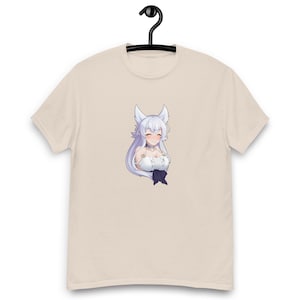 May include: A beige t-shirt featuring a cartoon anime character with white hair, fox ears, and a white dress. The character has a smiling expression and a dark blue bow. The t-shirt is hanging on a black hanger.