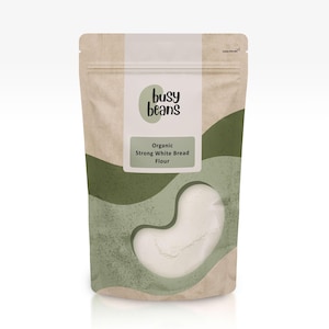 May include: A tan packet of Busy Beans organic strong white bread flour. The packaging features a green wave design and a bean-shaped window revealing the white flour. The label states "Organic Strong White Bread Flour."