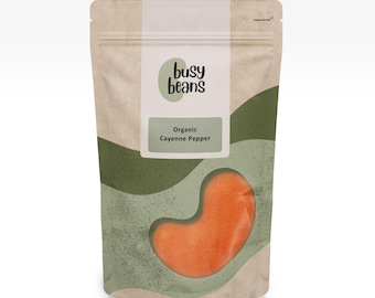 Puede incluir: Un paquete de pimiento de cayena orgánico de Busy Beans. La bolsa es de color beige con una ventana transparente que muestra el pimiento naranja. La etiqueta dice "Organic Cayenne Pepper". El fondo tiene formas abstractas verdes y grises.