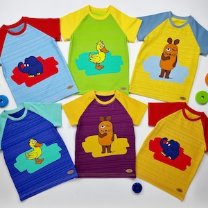 Könnte beinhalten: Sechs bunte T-Shirts mit verschiedenen Tiermotiven. Die Shirts sind alle kurzärmelig und haben einen Raglan-Ärmel. Die Tiere sind ein Entchen, ein Elefant und eine Maus.