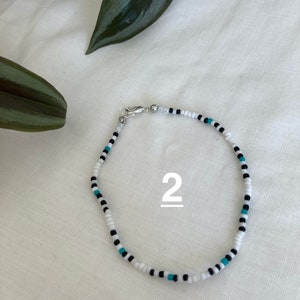 May include: White, black, and turquoise beaded bracelet with a silver clasp. The bracelet is labeled with the number "2".