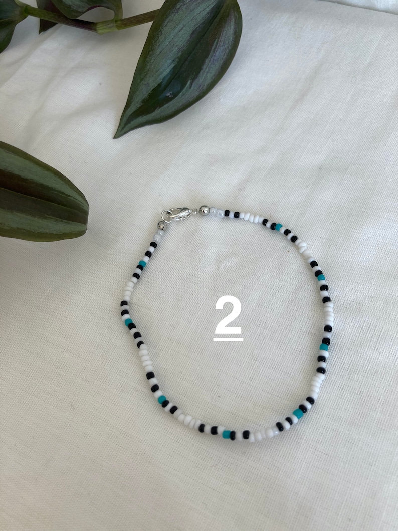 May include: White, black, and turquoise beaded bracelet with a silver clasp. The bracelet is labeled with the number "2".
