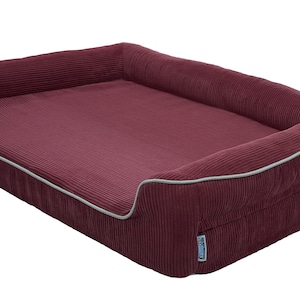 May include: A burgundy corduroy dog bed with a grey trim. The bed has a raised edge and a soft, comfortable surface.