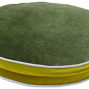 May include: A round, green velvet cushion with a yellow and white trim. The cushion is perfect for adding a touch of color and comfort to any room.
