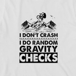 May include: White t-shirt with a black graphic of a mountain biker performing a stunt. The text reads "I don't crash I do random gravity checks."