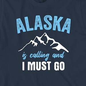 May include: A navy blue t-shirt with a white mountain graphic and the text "Alaska is calling and I must go" in blue.