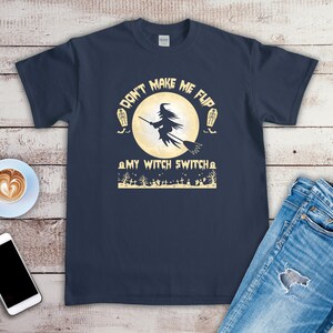 May include: Navy blue t-shirt with a Halloween-themed graphic. The design features a witch on a broom in front of a full moon, with the text "DON'T MAKE ME FLIP MY WITCH SWITCH". Tombstones and trees are also included in the design.