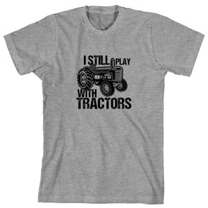 May include: A grey t-shirt with the text "I Still Play With Tractors" and a black and white illustration of a tractor.