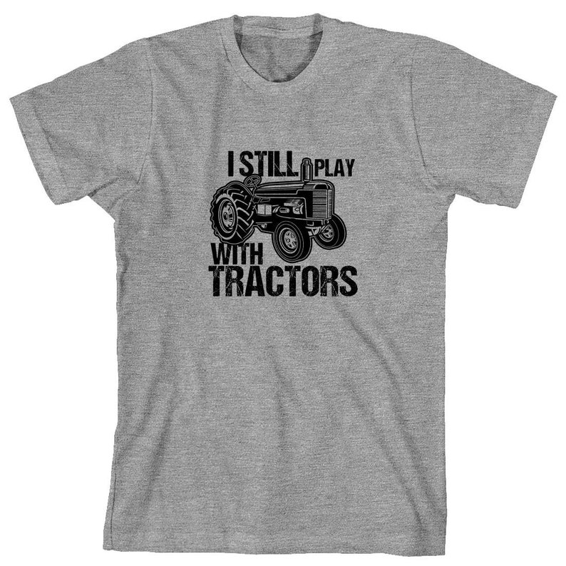 May include: A grey t-shirt with the text "I Still Play With Tractors" and a black and white illustration of a tractor.