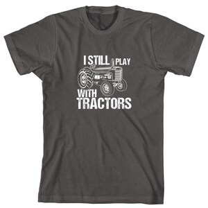 May include: A dark grey t-shirt with a white graphic of a tractor and the text "I Still Play With Tractors".
