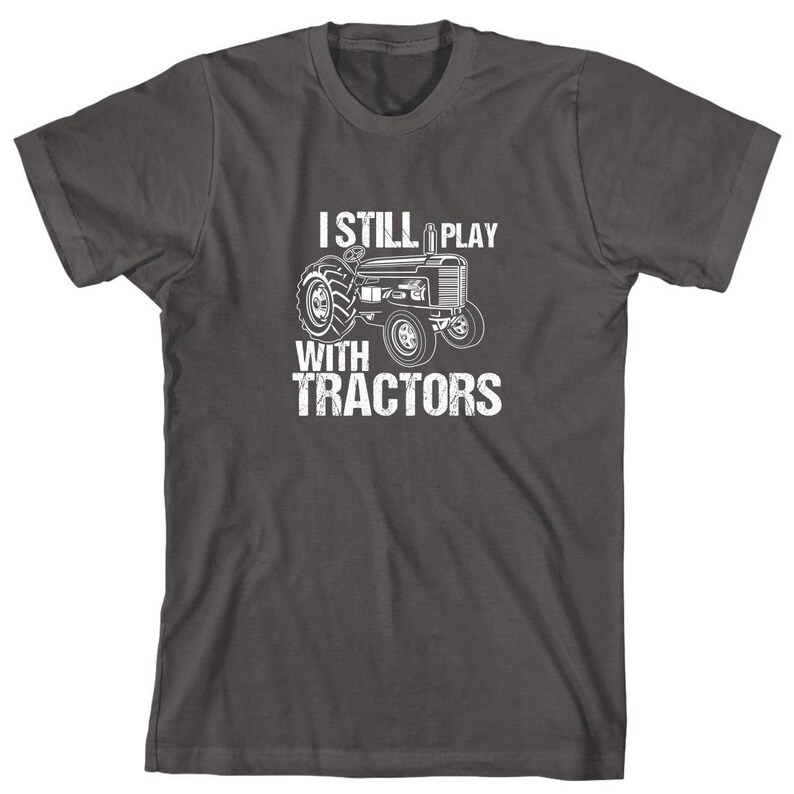 May include: A dark grey t-shirt with a white graphic of a tractor and the text "I Still Play With Tractors".
