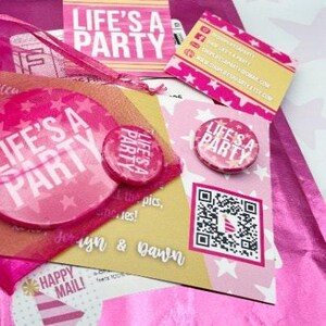 May include: A collection of pink and white party-themed stationery items. The items include buttons, cards, and stickers with the text "LIFE'S A PARTY" and star patterns. A QR code is also visible.