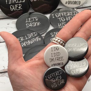 May include: A collection of round, black and white buttons with humorous phrases. The buttons have text like "Finally Over," "Let's Drink," and "I Offered to Key His Car." Some buttons are gray, and one is white.