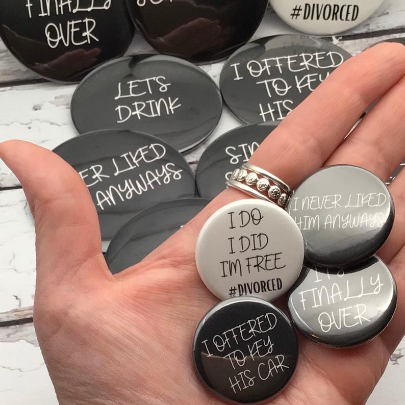 May include: A collection of round, black and white buttons with humorous phrases. The buttons have text like "Finally Over," "Let's Drink," and "I Offered to Key His Car." Some buttons are gray, and one is white.
