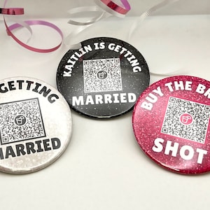 May include: Three round buttons with glitter backgrounds and black text. The buttons read "I'm getting married", "Kaitlin is getting married", and "Buy the bride a shot". Each button has a QR code with a cocktail glass icon.