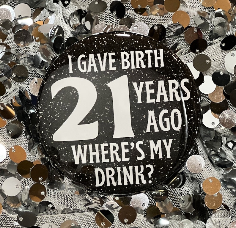 May include: A black and white button with glitter, featuring the text "I gave birth 21 years ago where's my drink?"