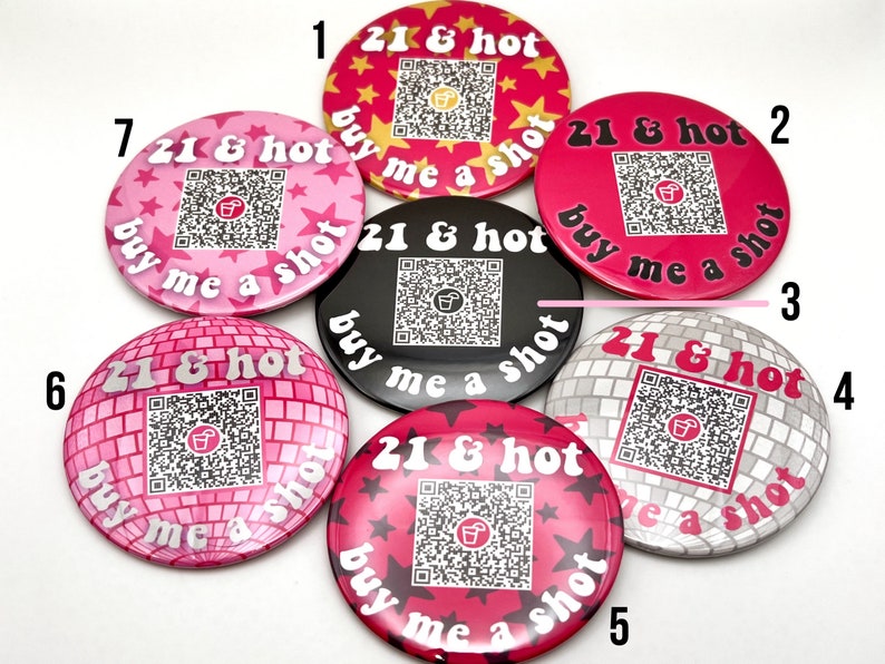 Puede incluir: Siete botones redondos de color rosa y blanco con un c&oacute;digo QR en blanco y negro y el texto "21 & hot buy me a shot" impreso en ellos. Los botones est&aacute;n numerados del 1 al 7.